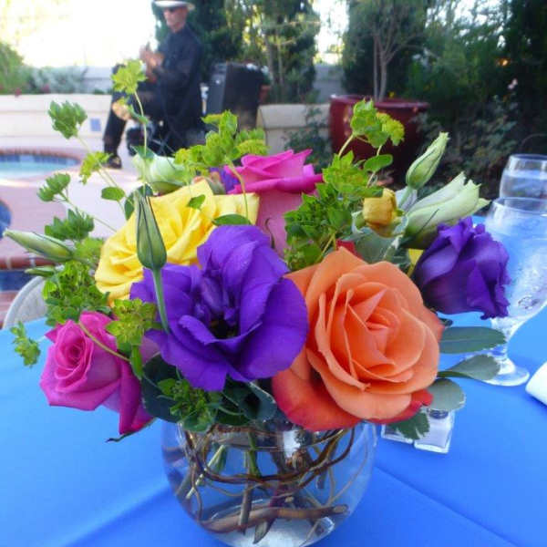 Small round centerpiece with orange, yellow, pink, and purple flowers in a clear bowl vase