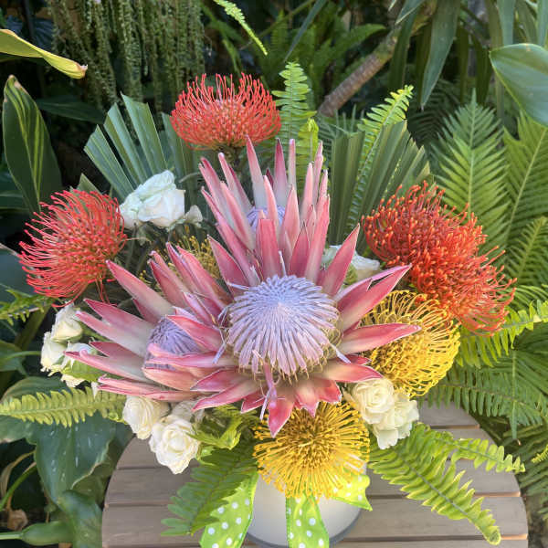 Tropical bouquet with pink protea, orange pincushion blooms, and white roses in a vase