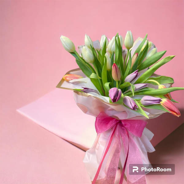 Bouquet of multicolored tulips wrapped in white paper with a pink ribbon