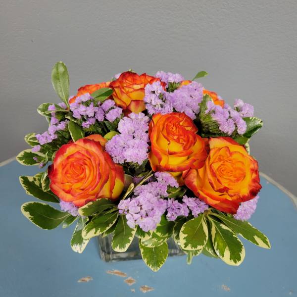 Orange roses and lavender filler flowers in a square glass vase
