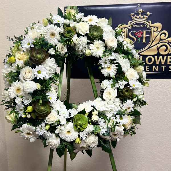White floral wreath on a stand with roses and daisies