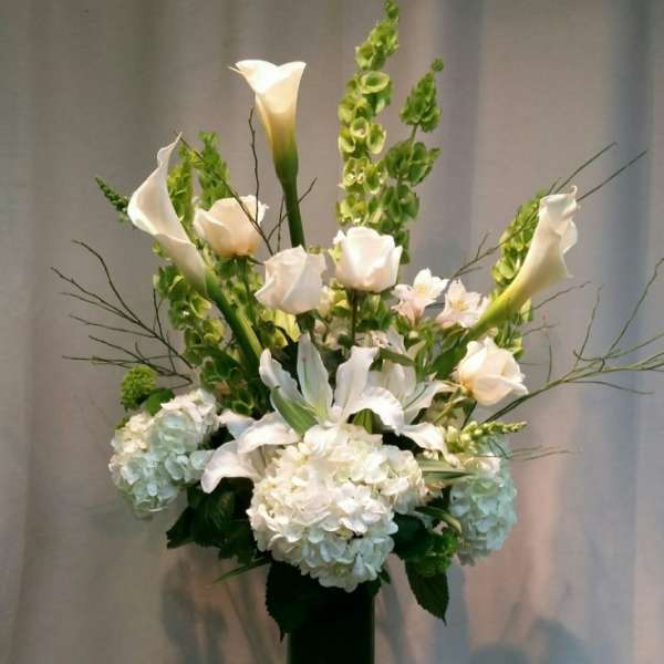 White calla lilies and hydrangeas in a tall glass vase