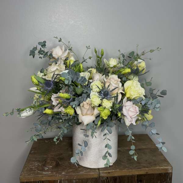 Mixed bouquet of pale roses and blue thistle in a white vase