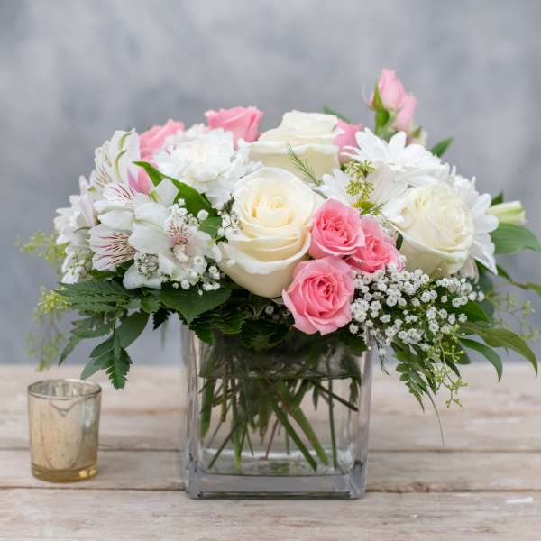 Pink and white roses arranged in a clear square vase