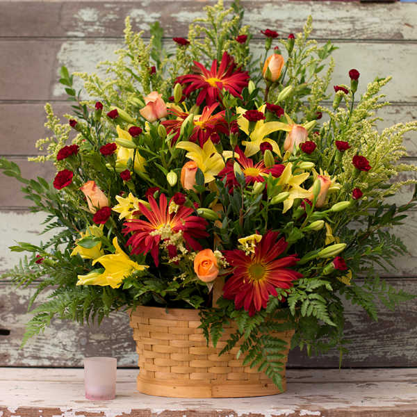 Mixed bouquet in a woven basket with red, yellow, and peach flowers
