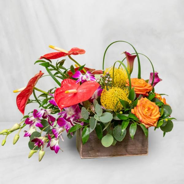 Tropical flower arrangement in a wooden box with red anthuriums and orange roses