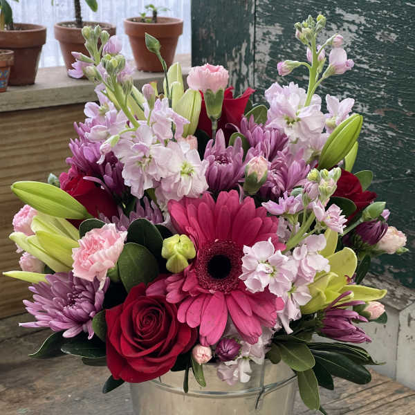 Mixed pink and red flowers arranged in a metal bucket