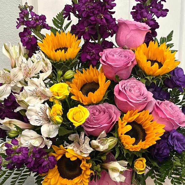 Pink roses, sunflowers, and purple flowers arranged in a pink box