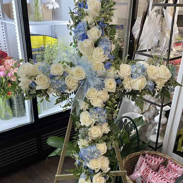 Cross-shaped floral tribute with white roses and blue hydrangeas on an easel