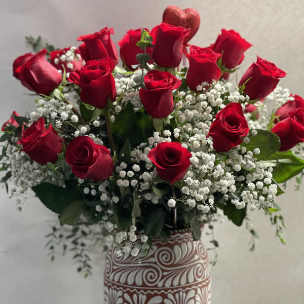 Red roses and baby's breath in a patterned vase with a heart pick