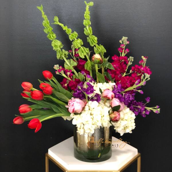 Mixed bouquet of red tulips, white hydrangeas, and purple flowers in a glass vase