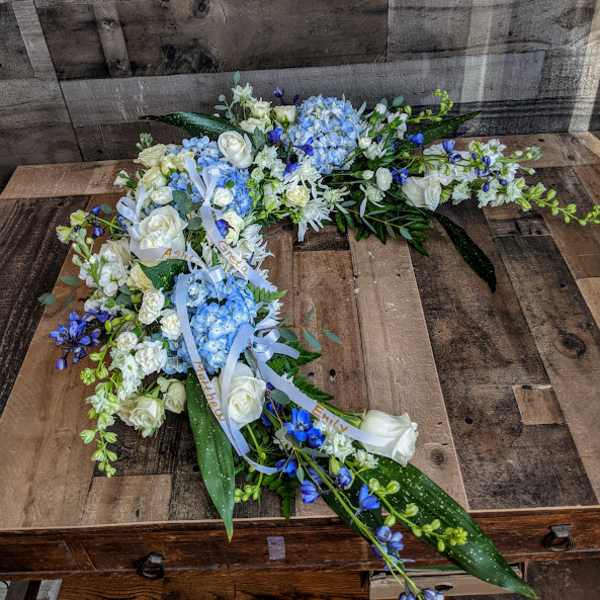Long blue and white floral spray with ribbons arranged on a wooden surface