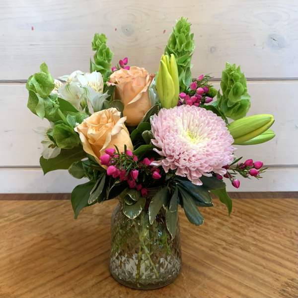 Mixed bouquet of roses, lilies, and a pink chrysanthemum in a glass vase