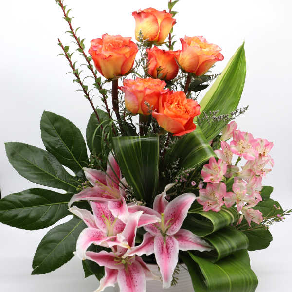 Orange roses and pink lilies arranged in a white vase