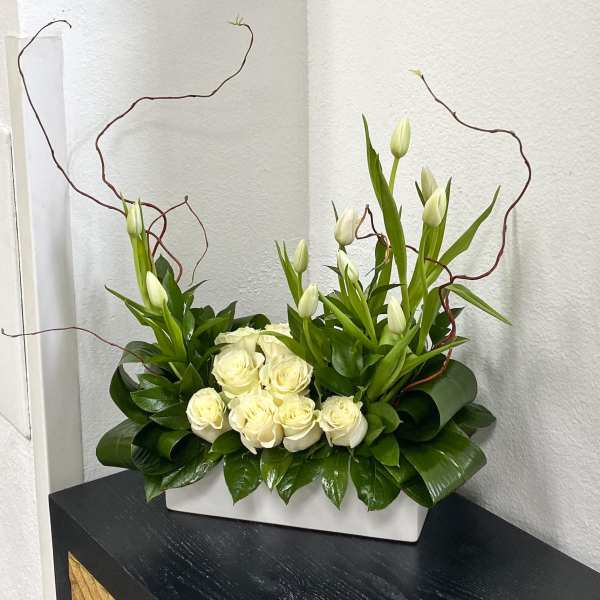 White roses and tulips arranged in a rectangular vase with curly branches