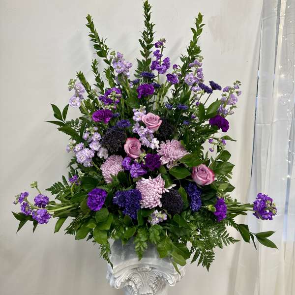 Tall purple and pink floral arrangement in a white pedestal vase