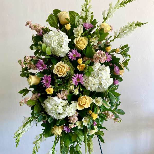 Standing floral spray with yellow roses, white hydrangeas, and purple blooms