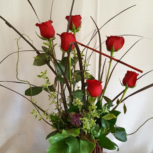 Tall arrangement of red roses in a woven basket with decorative branches