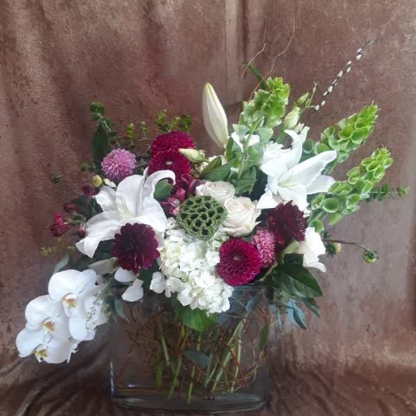 Mixed bouquet with white lilies, orchids, and burgundy blooms in a glass vase