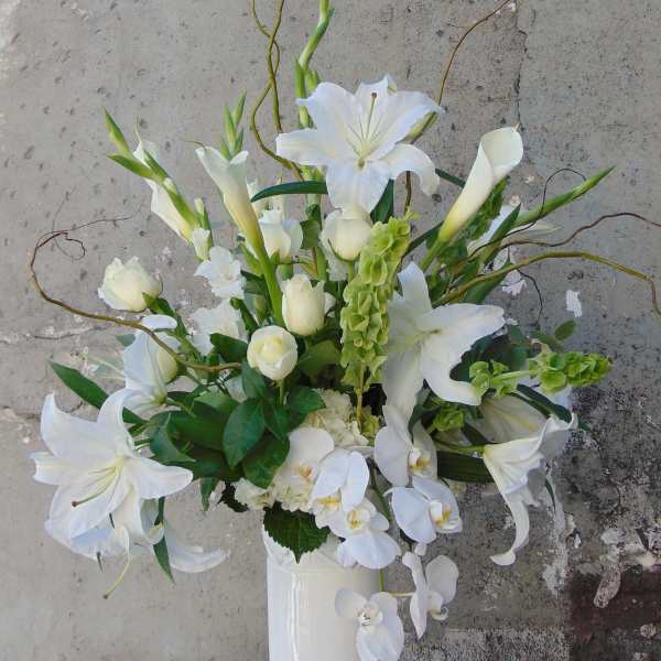 Tall white arrangement with lilies, calla lilies, roses, and orchids in a white vase
