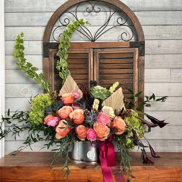Peach and pink rose arrangement in a metal container with ribbon