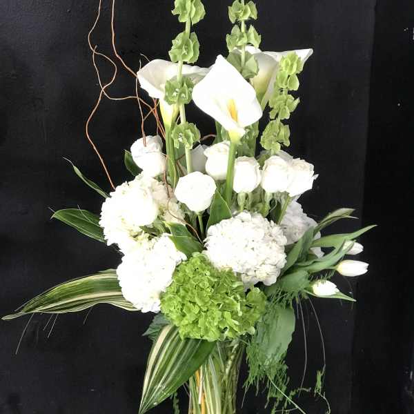 White calla lilies and hydrangeas in a glass vase with green accents