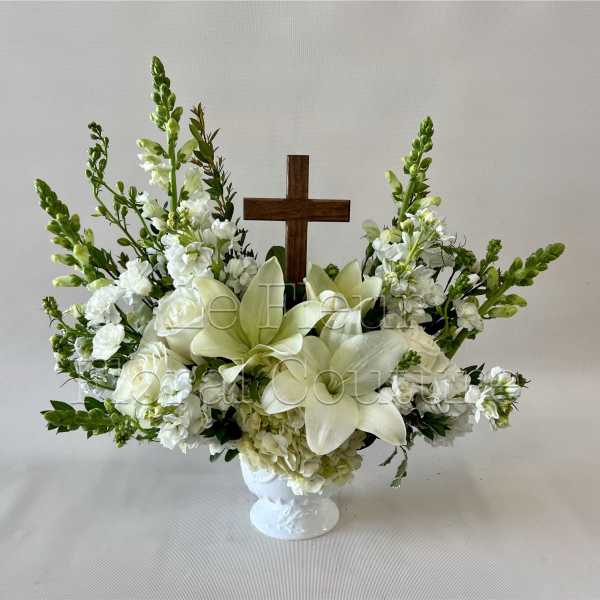 White floral arrangement with a wooden cross in a white vase