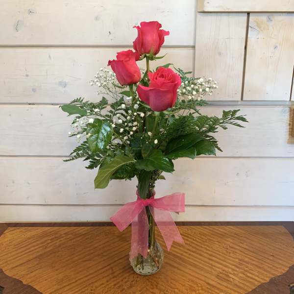 Three pink roses in a clear glass vase with a pink ribbon