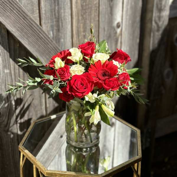 Red and white roses with a red gerbera daisy in a glass vase