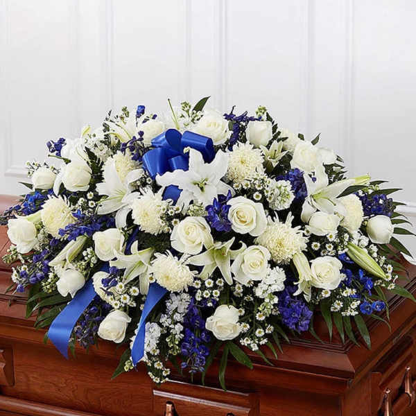 White and blue casket spray with roses, lilies, and ribbon on a polished wooden casket