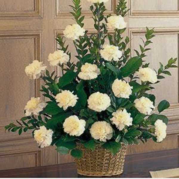 Tall basket arrangement of white carnations with layered foliage.