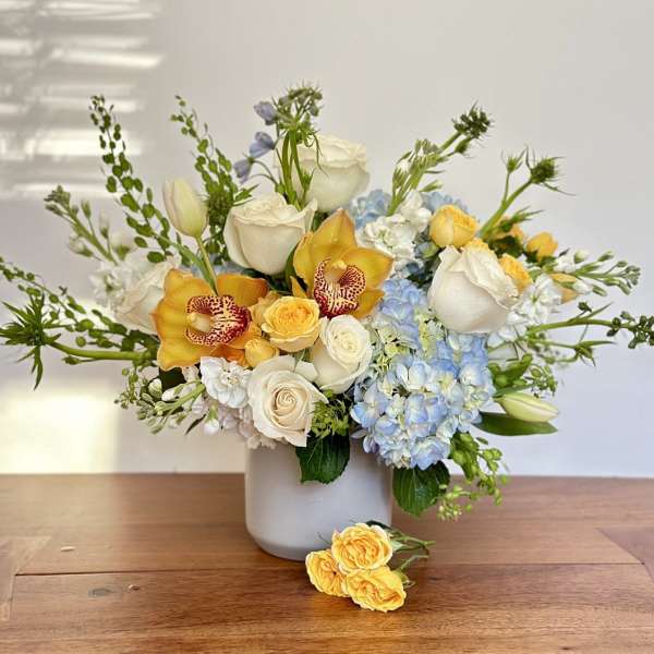 Bouquet of white roses, blue hydrangeas, and yellow orchids in a white vase