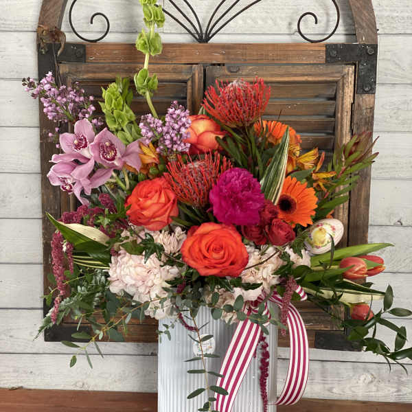 Colorful mixed flower arrangement in a clear ribbed vase with a striped ribbon
