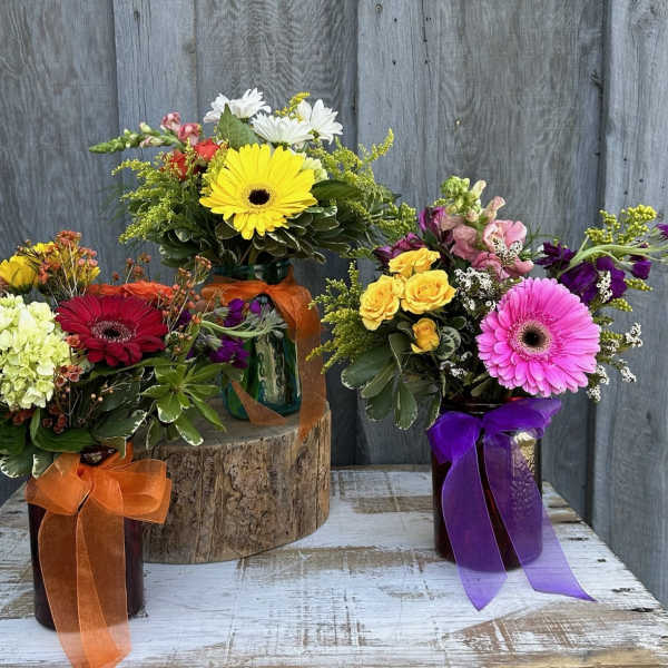 Three colorful flower arrangements in ribbon-tied vases on a rustic table