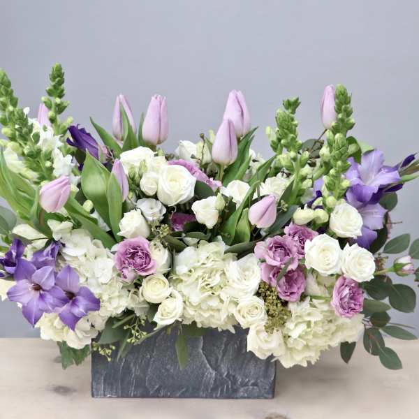 Rectangular arrangement of white and lavender flowers, including tulips and roses, in a gray stone container