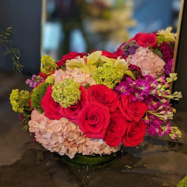 Bouquet of red roses, pale hydrangeas, and yellow lilies in a low glass vase