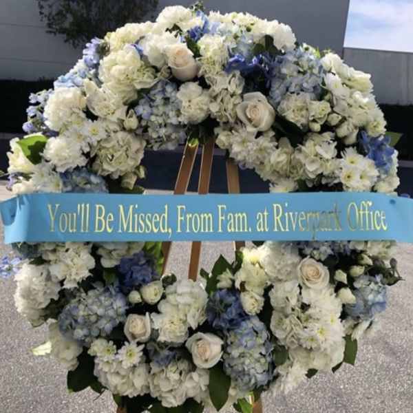 Large white and blue funeral wreath on an easel with a memorial ribbon