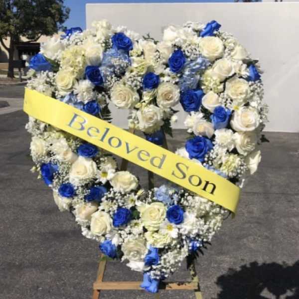 Heart-shaped floral wreath with blue and white roses and a yellow ribbon