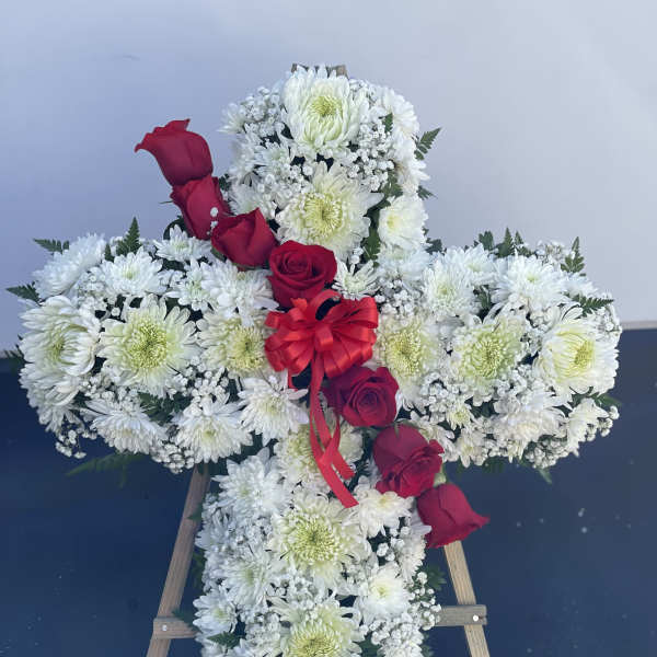Cross-shaped floral tribute with white flowers and red roses on a stand