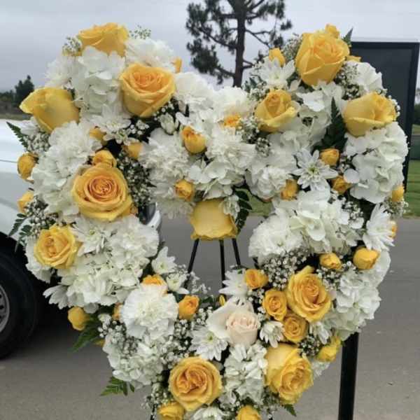 Heart-shaped floral wreath with yellow roses and white flowers on a stand
