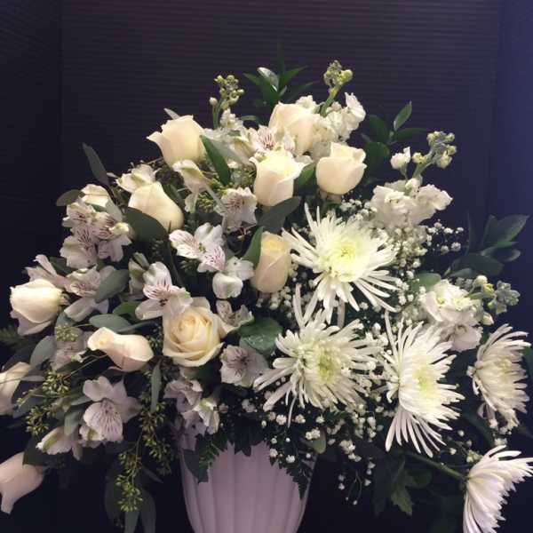 White roses and chrysanthemums arranged in a pale pedestal vase