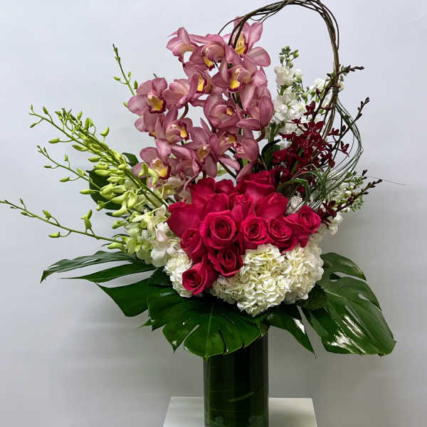 Tall bouquet of pink orchids, red roses, and white hydrangeas in a glass vase