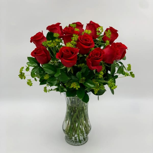Red roses arranged in a clear glass vase with green filler
