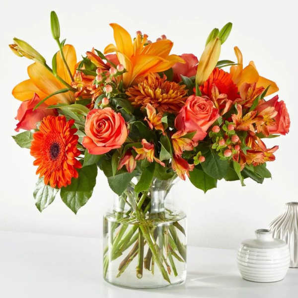 Orange lilies, roses, and gerbera daisies in a clear glass vase