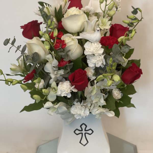 Red and white flower arrangement in a white vase with a cross emblem