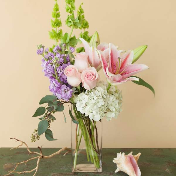 Pink lilies, roses, hydrangea, and purple stock in a glass vase