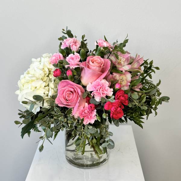 Pink roses, carnations, and white hydrangeas arranged in a clear glass vase