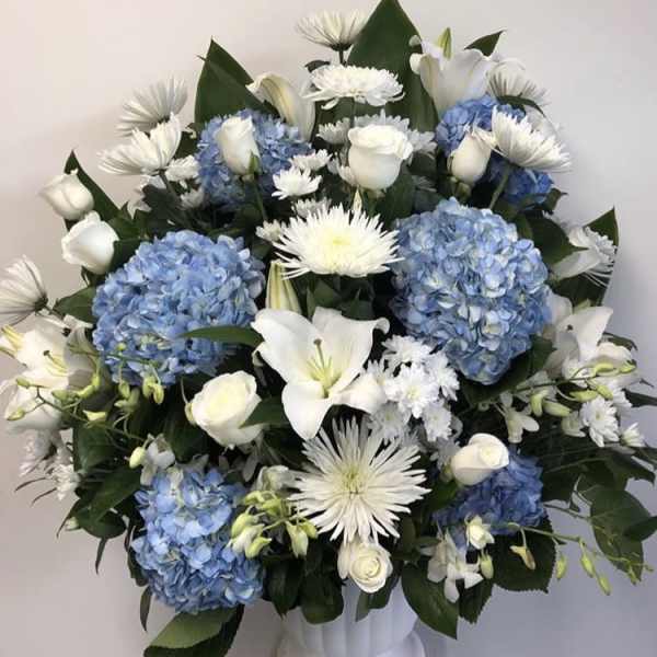 White lilies and roses with blue hydrangeas in a white vase
