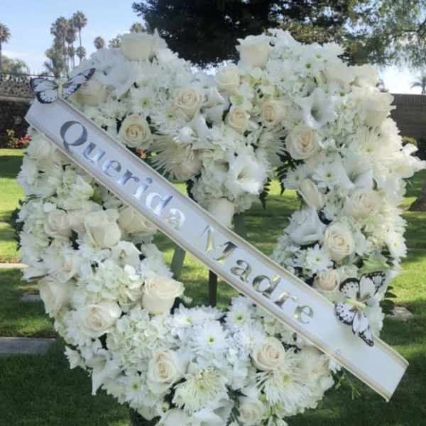White floral funeral wreath on an easel with a diagonal memorial ribbon