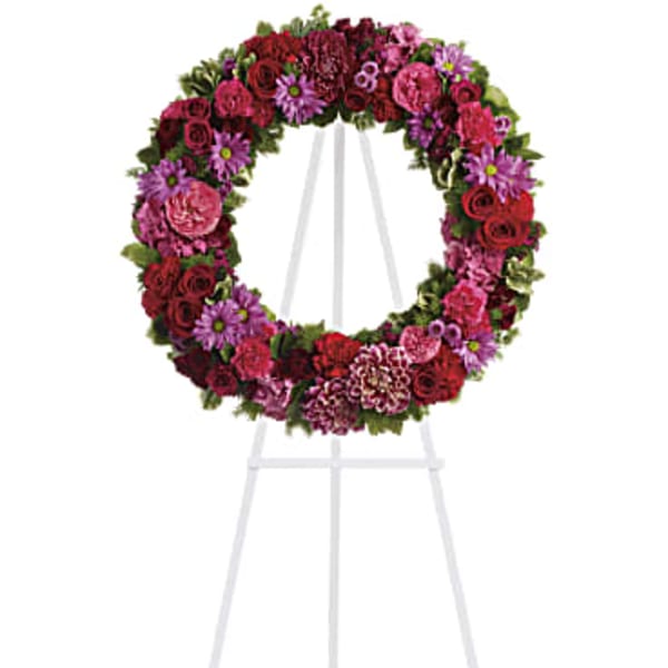 Circular floral wreath on a white easel with pink, red, and purple flowers